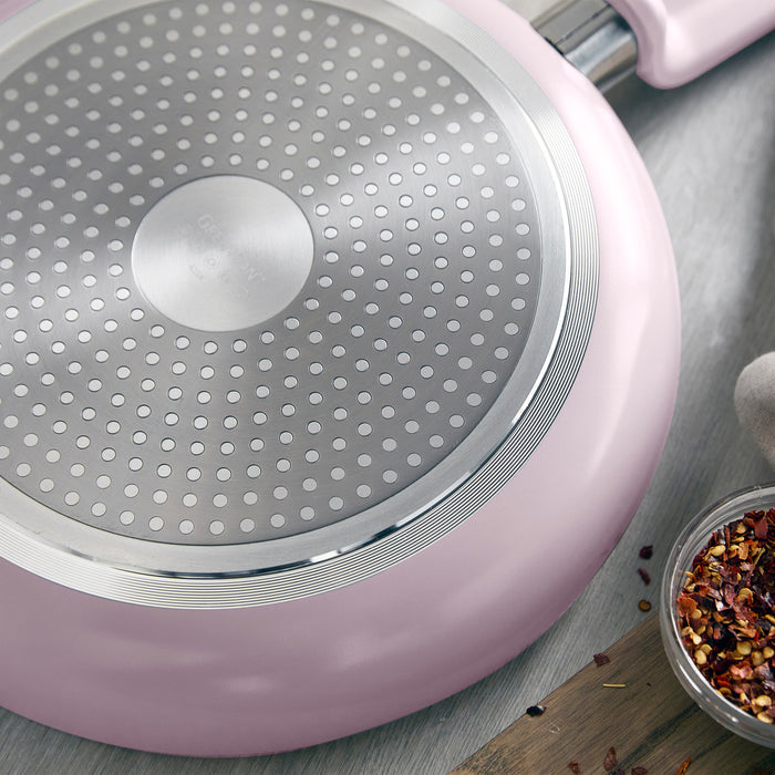 Pink 12-piece ceramic nonstick cookware set with dotted metal base, shown close up next to chili flakes.