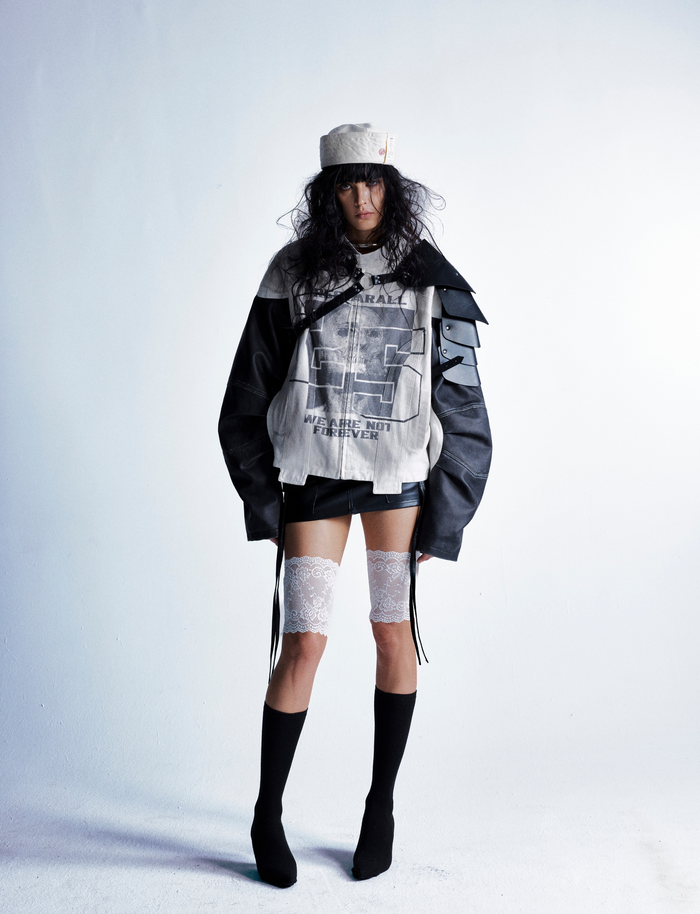 Full-body view of model wearing cream and black moto jacket with black shorts and boots