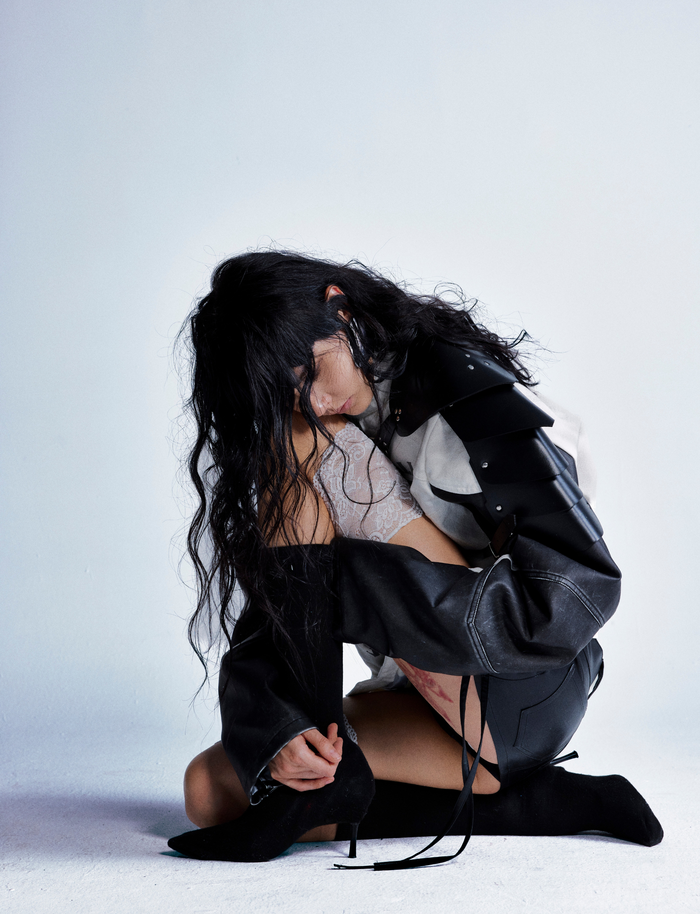 Model seated in cream and black skull graphic jacket with layered shoulder panels