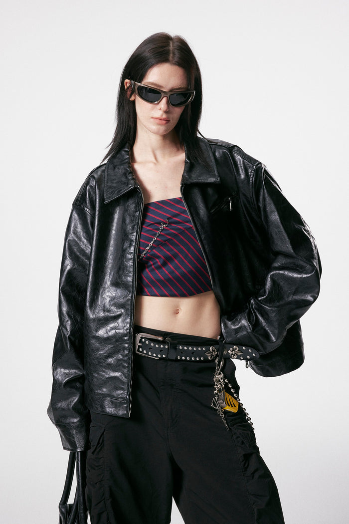 Model wearing black crinkle PU leather jacket over striped crop top and cargo pants