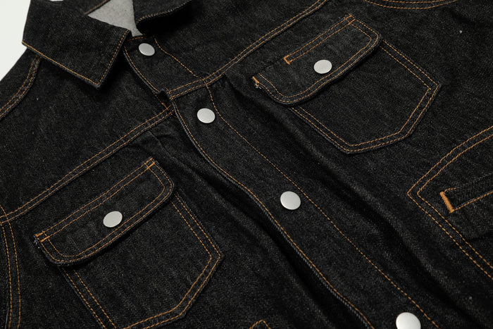 Close-up of the chest area on a black denim jacket with flap pockets and snap buttons