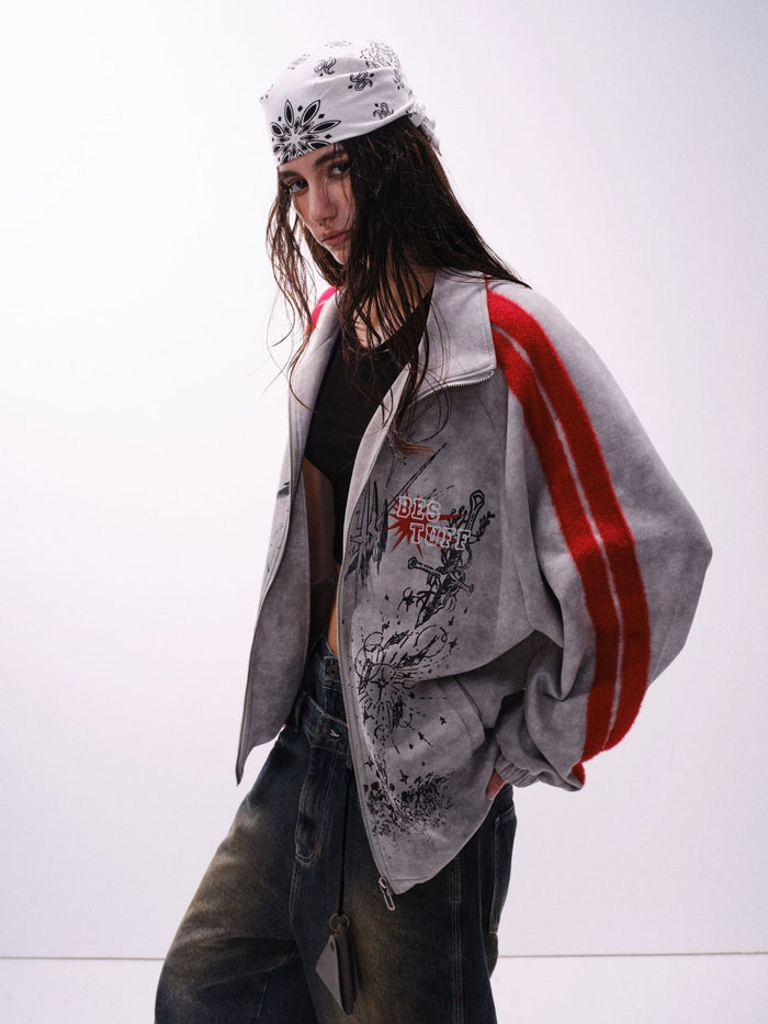 Three-quarter view of a gray graphic track jacket with red striped sleeves on a model wearing jeans