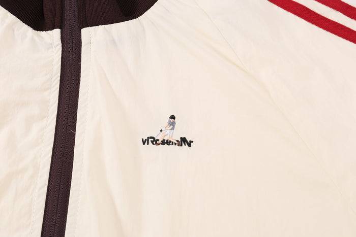 Close-up of front chest logo beside dark brown zipper on cream nylon jacket