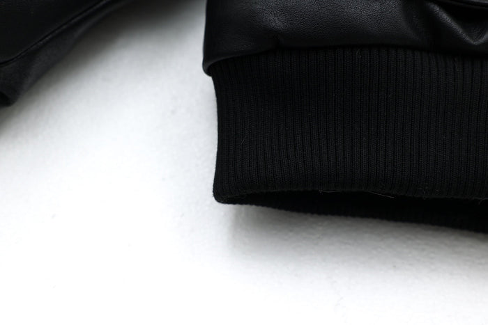 Close-up of black ribbed hem on bomber jacket with faux leather shell