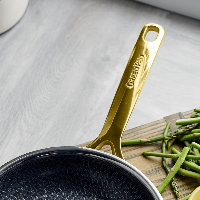 Gold ceramic nonstick 8 frypan with gold handle next to chopped asparagus on a wooden cutting board.