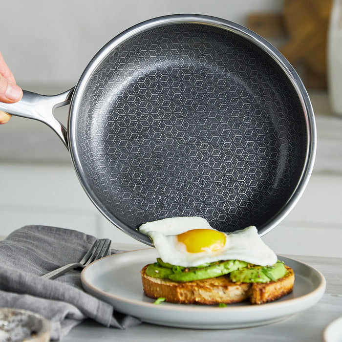 Hand holding a ceramic nonstick frypan above a plate with avocado toast and a fried egg.