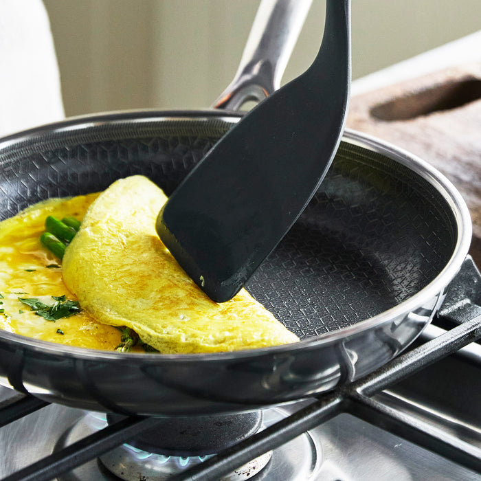 Spatula folding a veggie omelet in a grey ceramic nonstick frypan on a gas stove.