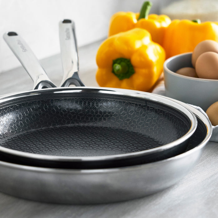 Three stacked ceramic nonstick frypans in different sizes next to bell peppers and eggs.