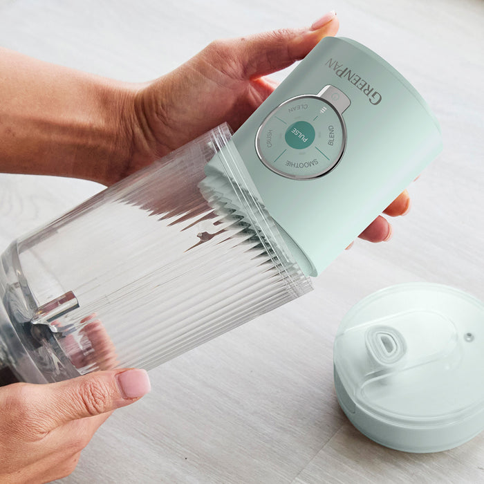 Someone assembling the Spin & Go Portable Blender | Seaside, connecting the base with control buttons to a clear ribbed blending cup on a light surface—ideal for convenient on-the-go blending.
