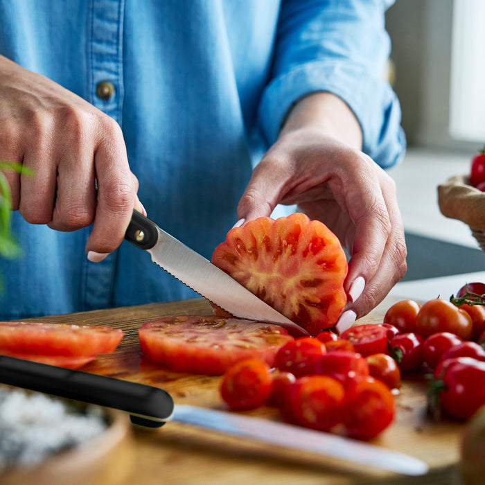 Person slicing tomato on a wooden cutting board with a knife.