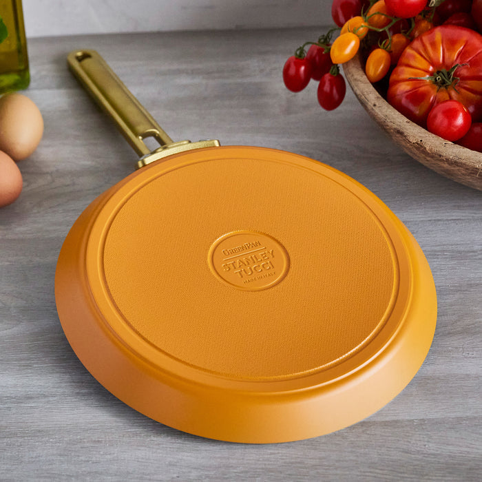 Yellow crepe pan with 'Stanley Tucci' branding on a wooden surface with tomatoes and eggs.