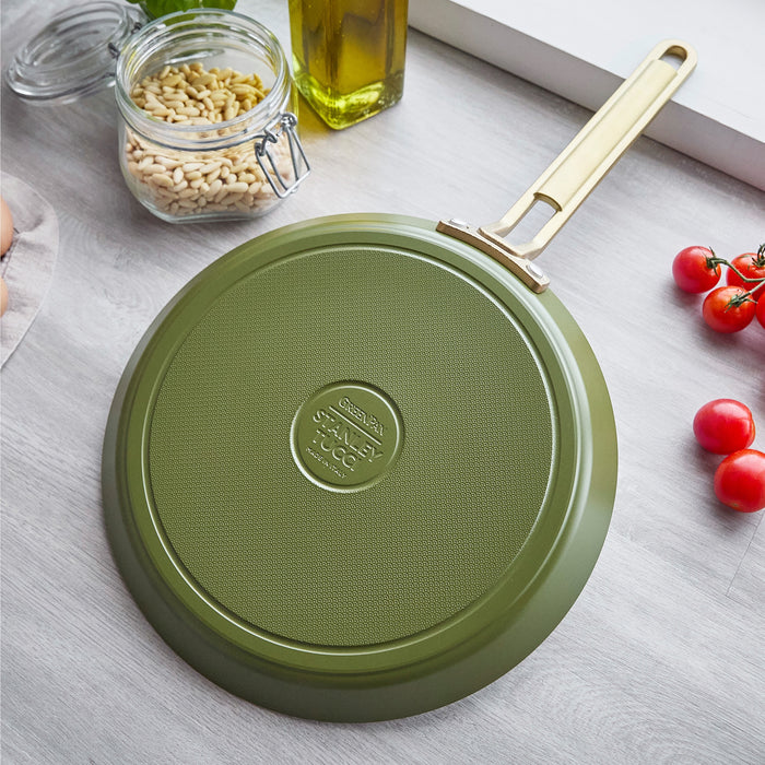 Green crepe pan with a gold handle on a light gray surface