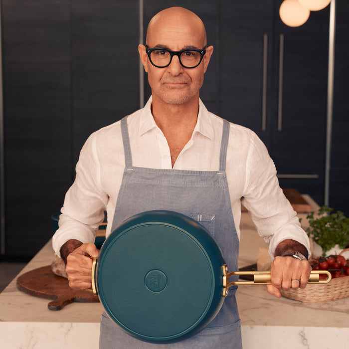 Man in glasses and apron holding a teal ceramic nonstick 3-piece cookware set, facing the camera.
