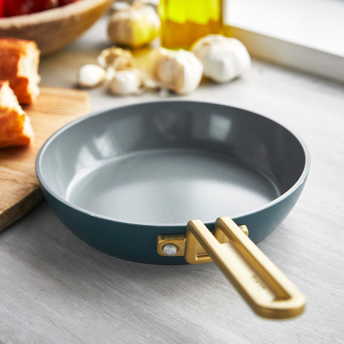 Ceramic nonstick mini cookware set in teal, three pieces, on a counter with bread, garlic, and oil.