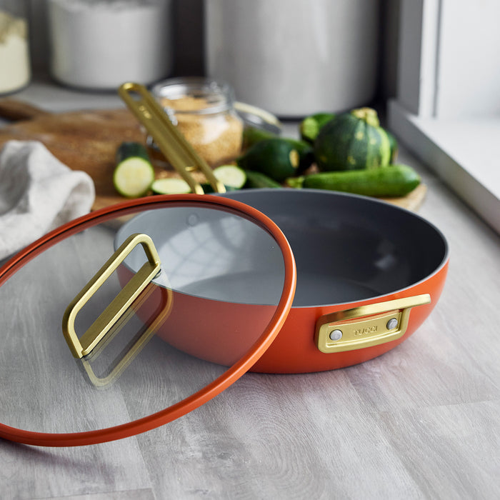 Ceramic nonstick 4.5-quart pan in Amalfi Sunset with glass lid on a counter, jars visible in the background.