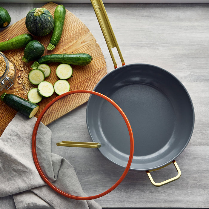 Ceramic nonstick 4.5-quart pan in Amalfi Sunset with lid next to zucchini on a wooden board.
