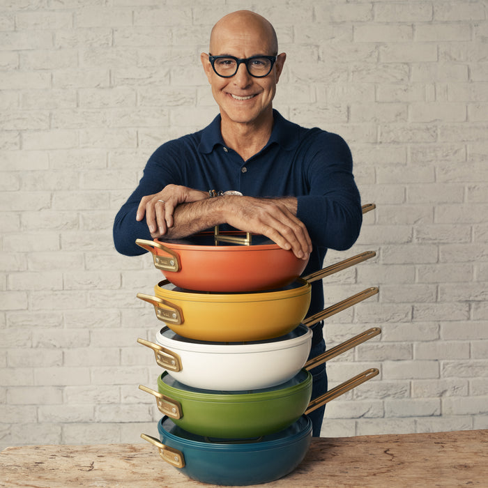 Man in glasses standing behind stacked white ceramic nonstick pans, Stanley Tucci™ 4.5-quart model visible.