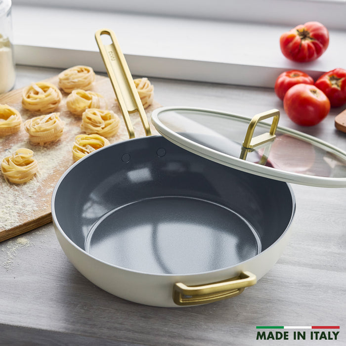 Ceramic nonstick pan on a counter near pasta nests and tomatoes, with Made in Italy visible.