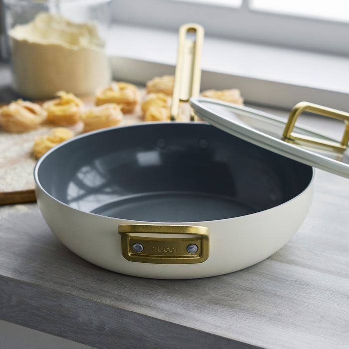 White ceramic 4.5-quart pan with lid on a kitchen counter beside pastries.