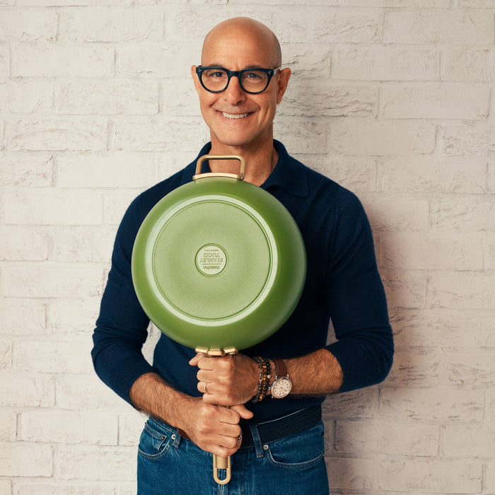 Stanley Tucci holding a green pan against a light brick wall
