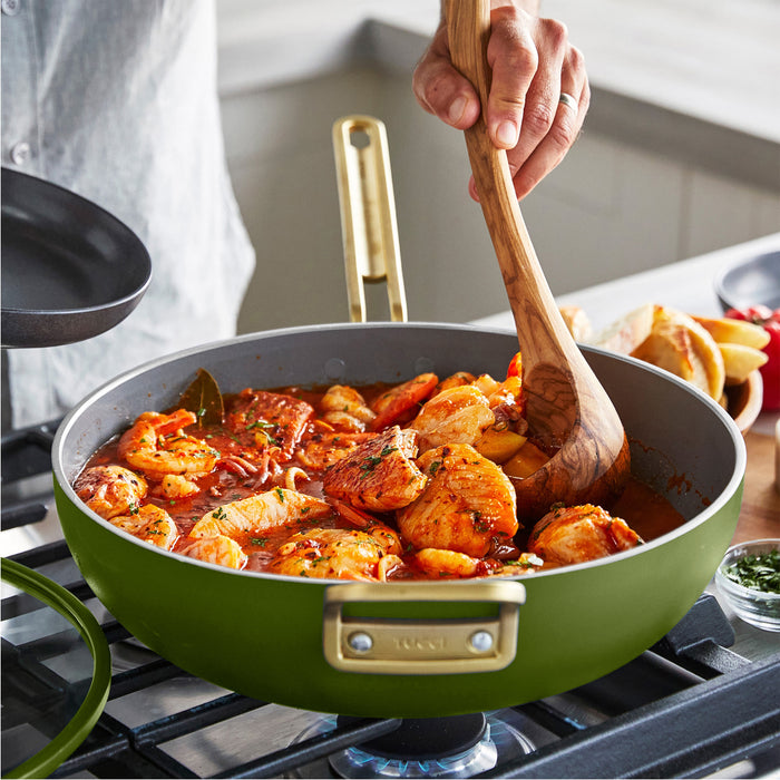Green saute pan with a seafood dish on a stove, wooden spoon stirring