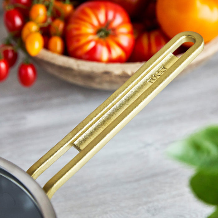 Stainless steel saucepan with champagne gold handles, 4-quart size; tomatoes in the background.