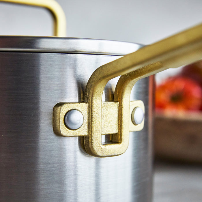 Stanley Tucci 4-quart nonstick saucepan with champagne-colored handles, blurred red and orange background.