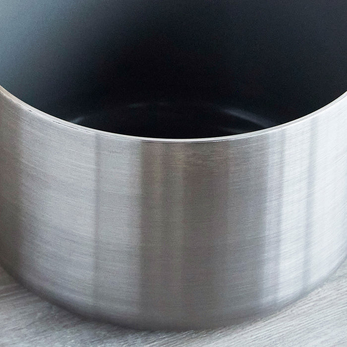 Stainless steel saucepan with ceramic nonstick interior and champagne handles on a wooden surface.