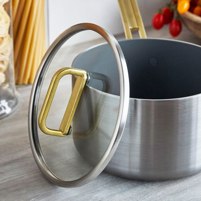 4-quart saucepan with champagne-colored handles on a kitchen counter beside uncooked pasta and fresh vegetables.
