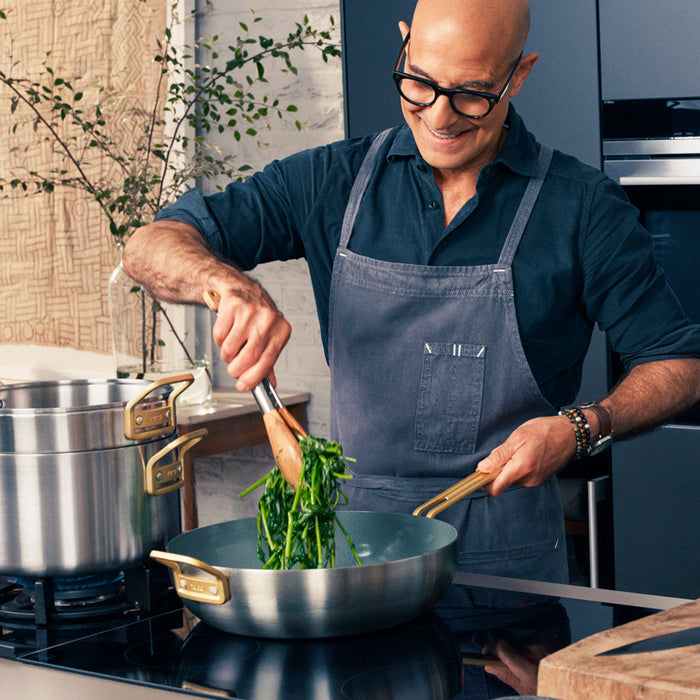 Man cooking greens in a stainless Stanley Tucci 4.5-quart pan on a modern stovetop, wearing an apron.