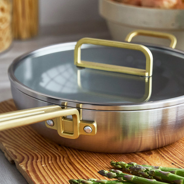 Stainless steel nonstick pan with lid on a board beside asparagus spears.