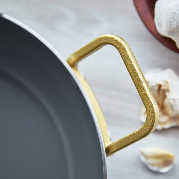 Stainless steel ceramic nonstick pan with lid beside garlic on a light surface.