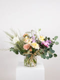 Heartfelt bouquet of pastel seasonal flowers and greenery presented in a glass vase or wrapped in kraft paper to express comfort for the loss of a pet.