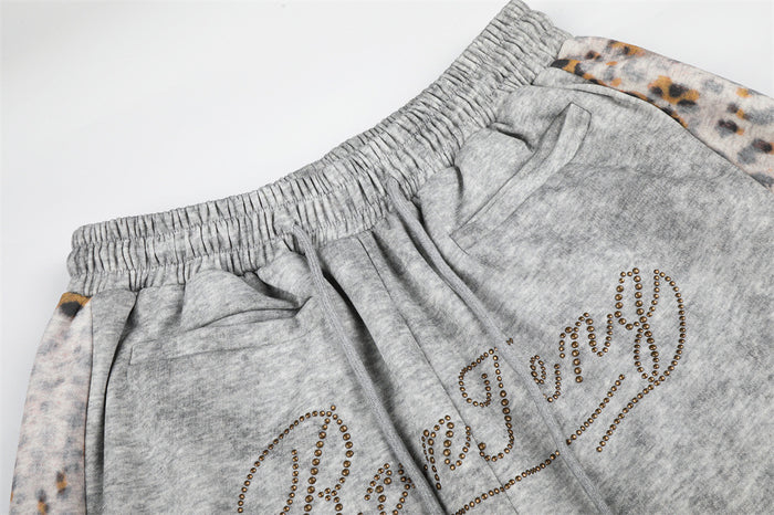 Close-up of gray sweatpants waistband, drawstring, pockets, and rhinestone script detail