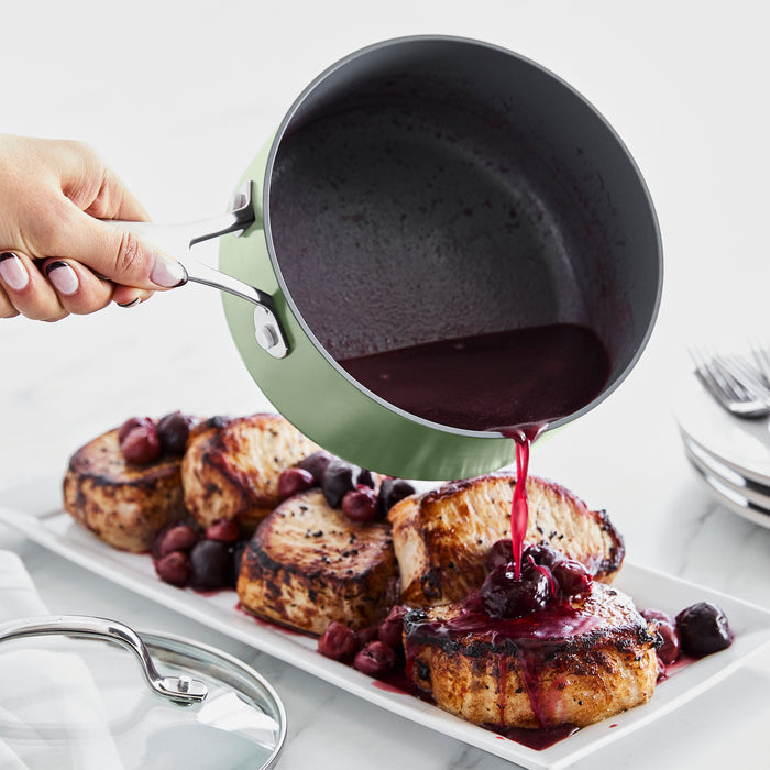 Sauce being poured over grilled pork chops from a gray ceramic saucepan onto a white plate.