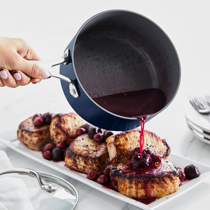 Sauce being poured from a grey ceramic nonstick saucepan onto grilled pork chops on a white platter.