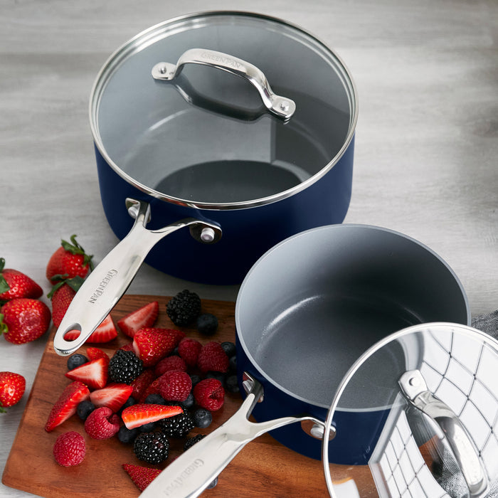 Two gray ceramic nonstick saucepans with lids beside assorted berries on a wooden cutting board. Set of two.