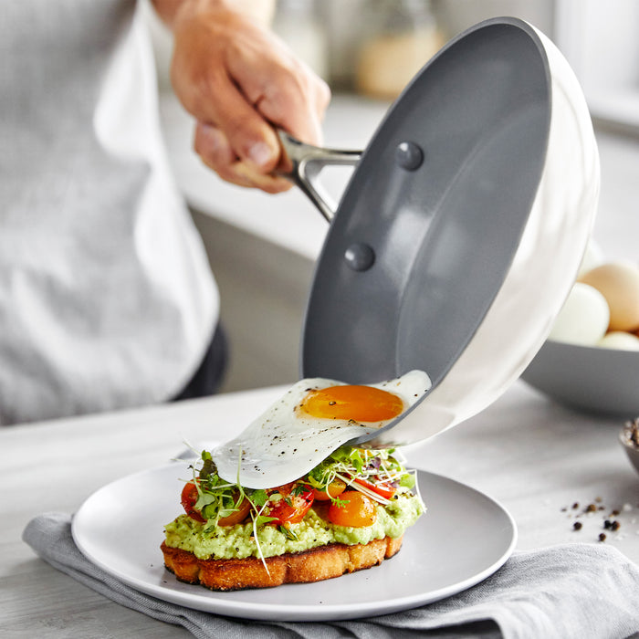 Person sliding a fried egg from a frypan onto avocado toast