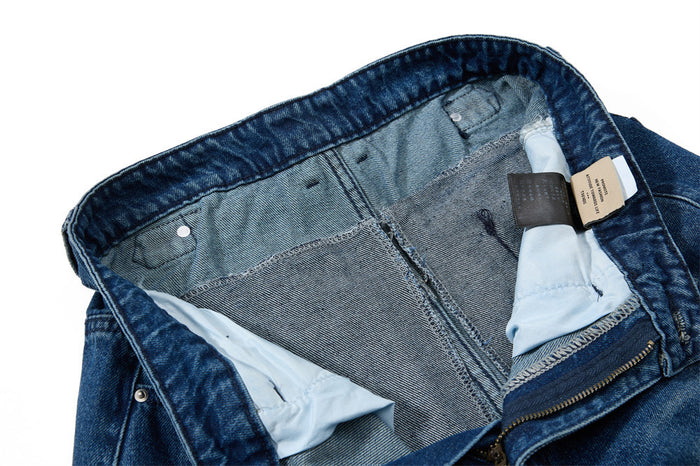 Inside waistband view of blue jeans with lining, stitching, and care tag