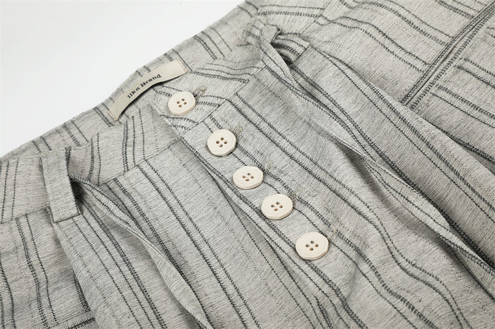 Close-up of four-button front fly, waistband, and pleats on gray striped trousers