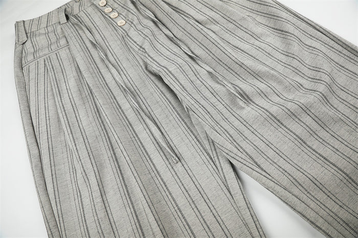 Angled view of gray striped wide-leg trousers showing front pleats and button fly